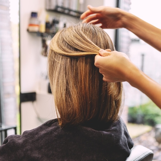 Cheveux blonds : coupe au carré et soin en salon de coiffure Coiffeur examinant une mèche de cheveux blonds lisses lors d'une coupe au carré dans un salon professionnel.